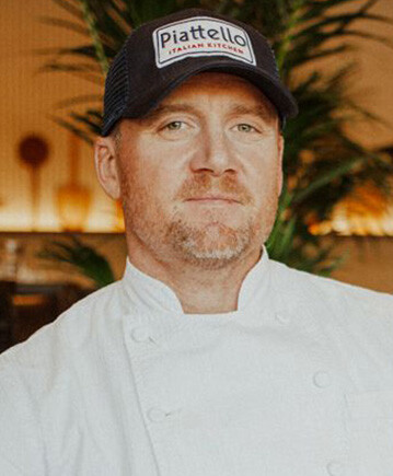 Headshot of Scott Lewis in a Chef's Coat and Piatello baseball cap